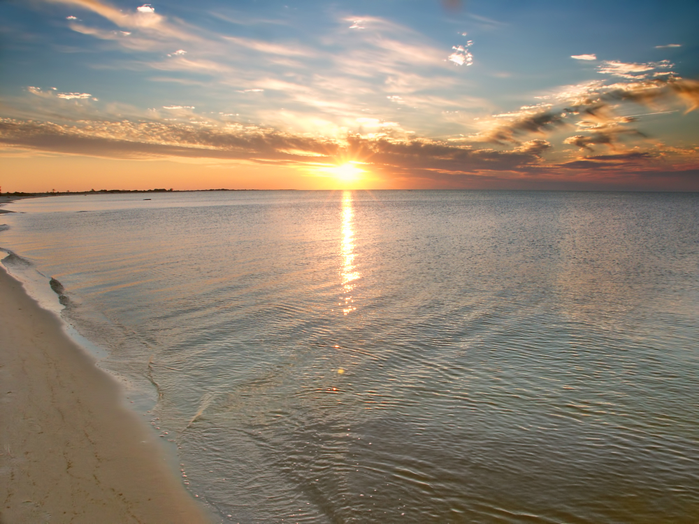 The sun sets over the ocean under gray and golden clouds