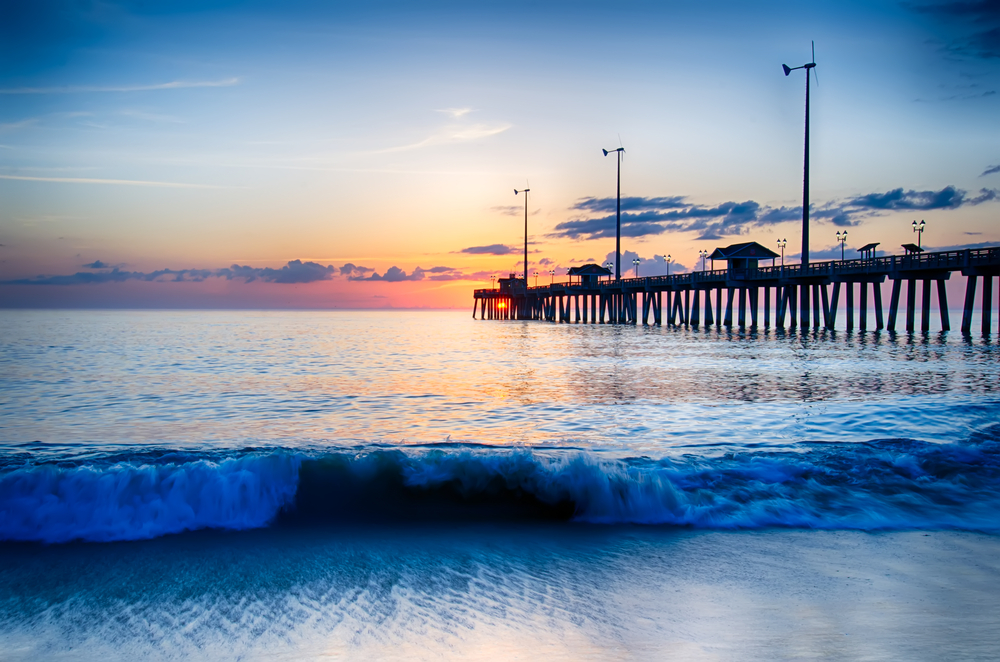 The rising sun peeks through clouds and is reflected in waves by the Nags Head fishing pier on the outer banks of North Carolina