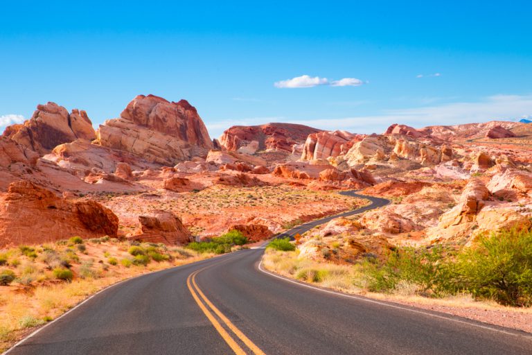 A paved road marks a path through large red rock formations in a desert landscape.