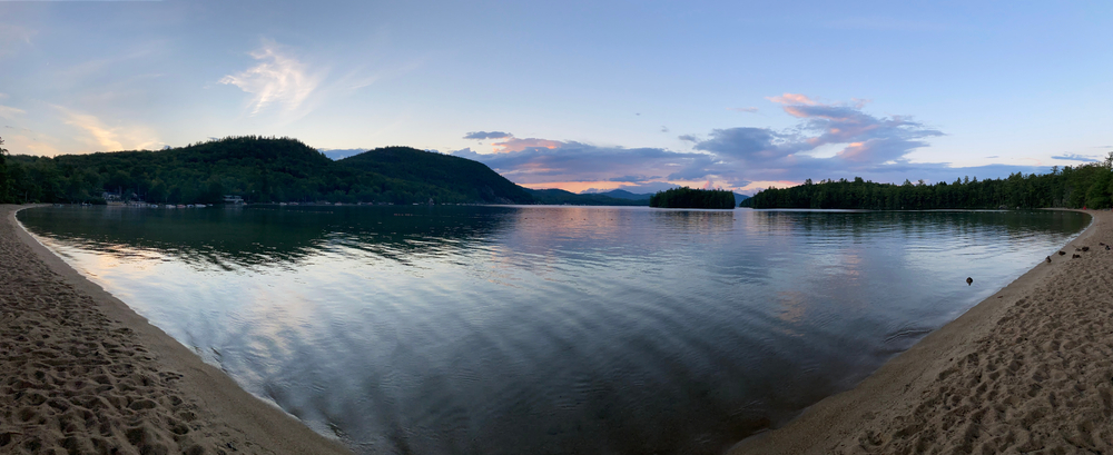 Bristol, New Hampshire (NH) / USA - August 21, 2020: Wellington State Park swimming lake beach panoramic at sunset with ducks on edge of Follansbee cove with sugarloaf mountain in background. J