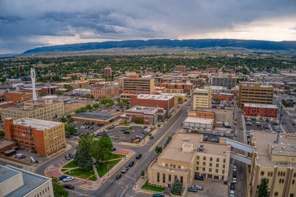 Aerial view of cityscape with multiple lane roads and a park in the foreground. Trees and a mountain range sit in the distance under gray-purple clouds.