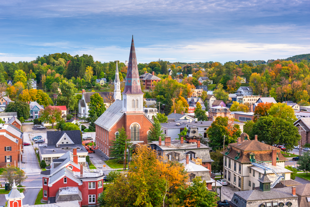 A brick building with a white and black tower sit in the middle of a city and trees.