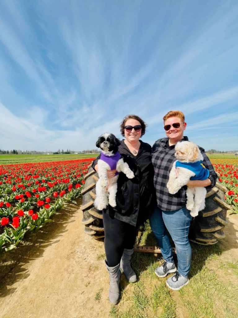 Couple holds their shih tzus while standing in a flower field