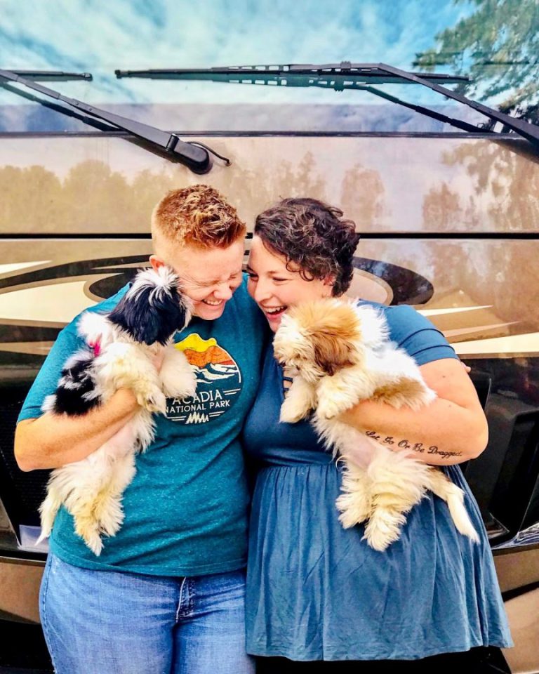 Couple holds their two shih tzus standing in front of their RV.