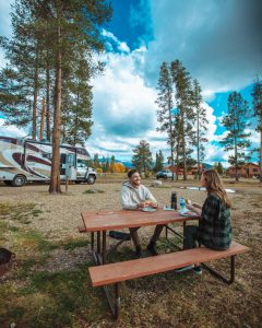 couple sitting at a picnic table with an RV parked in the background