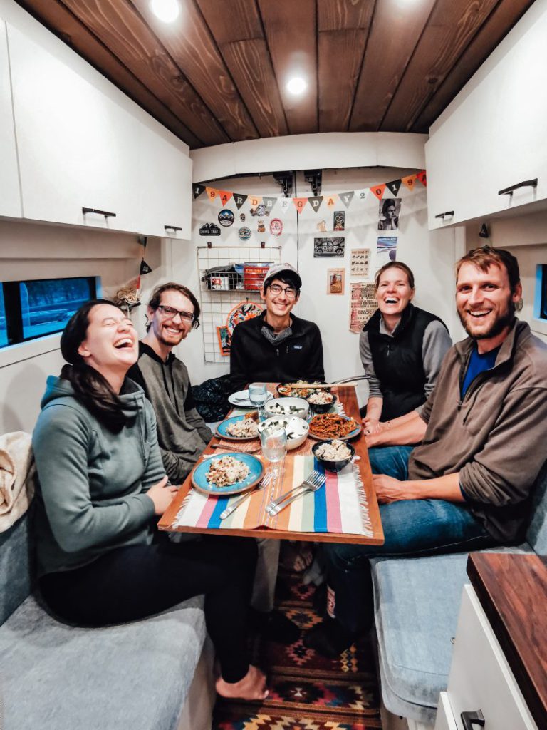 group of friends sits around table of a campervan