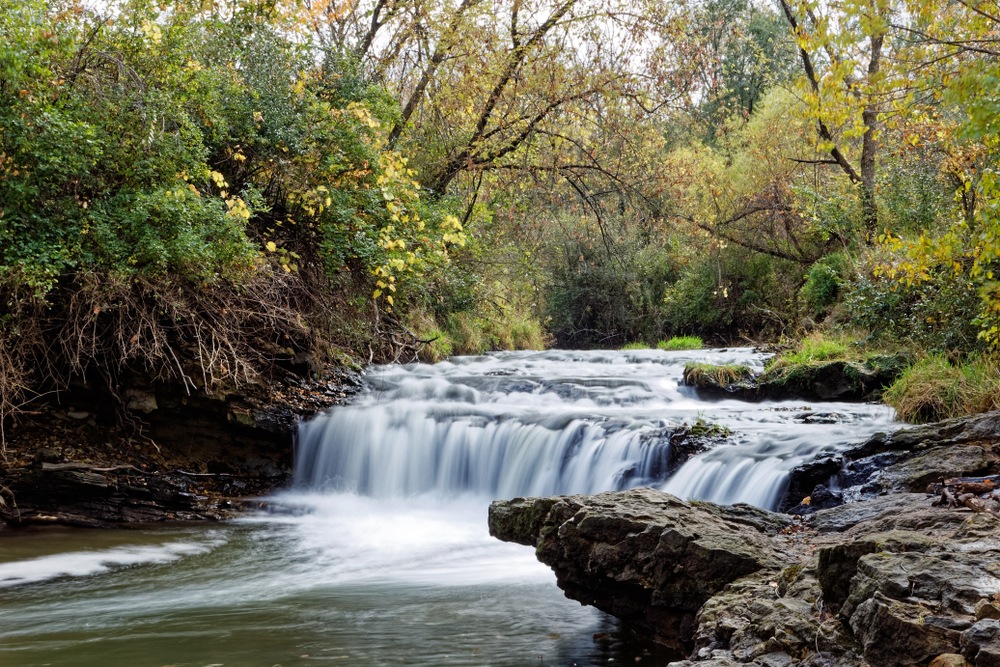 The water flows over the lower waterfall in Briggs Woods Park. The waterfall is surrounded by fall colors.