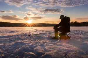 Silhouette of a man ice fishing on a lake in Norway at sunset.