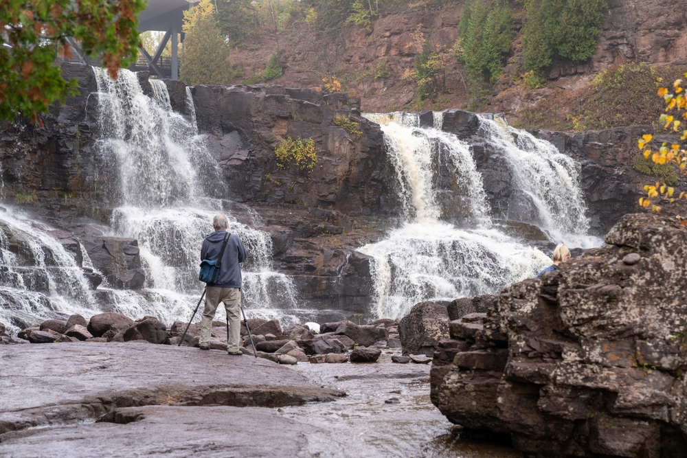 Minnesota, USA - October 6, 2021: Male photographer uses a tripod to take long exposure photos of Gooseberry Falls waterfall on a gloomy fall day
