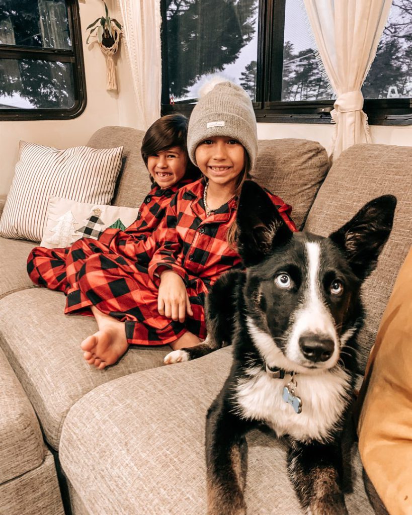 Two children in matching gingham pj's with their dog sit on a couch