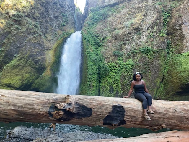 Woman sits on a log with a waterfall behind her