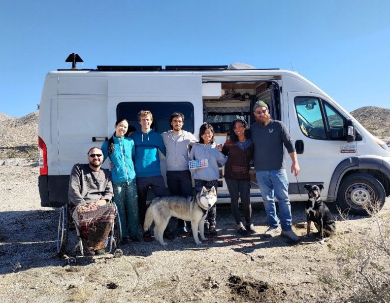 Group of people and dog stand outside a campervan at an RV meetup