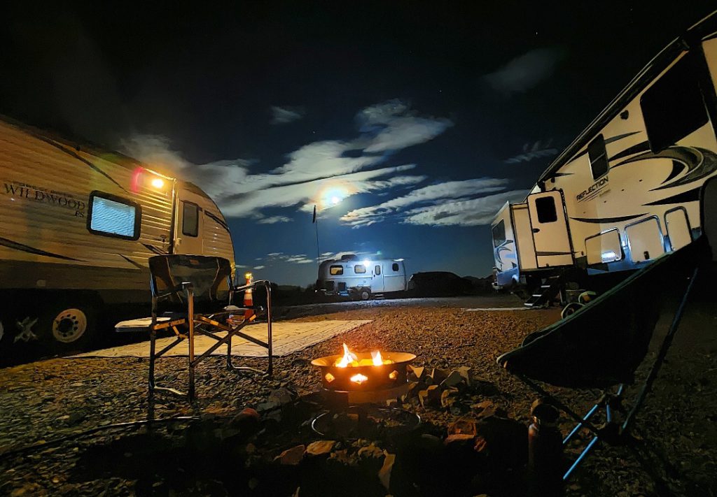 Group of Class C RVs parked near each other around a campfire at night