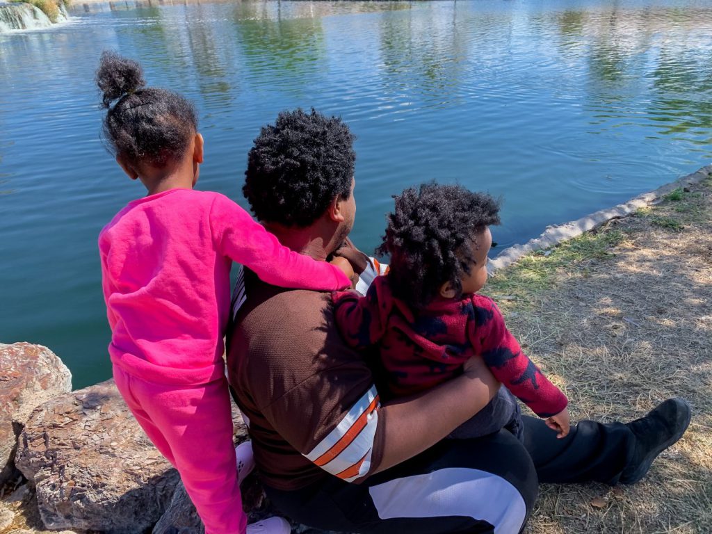 man with his two children looking into a body of water
