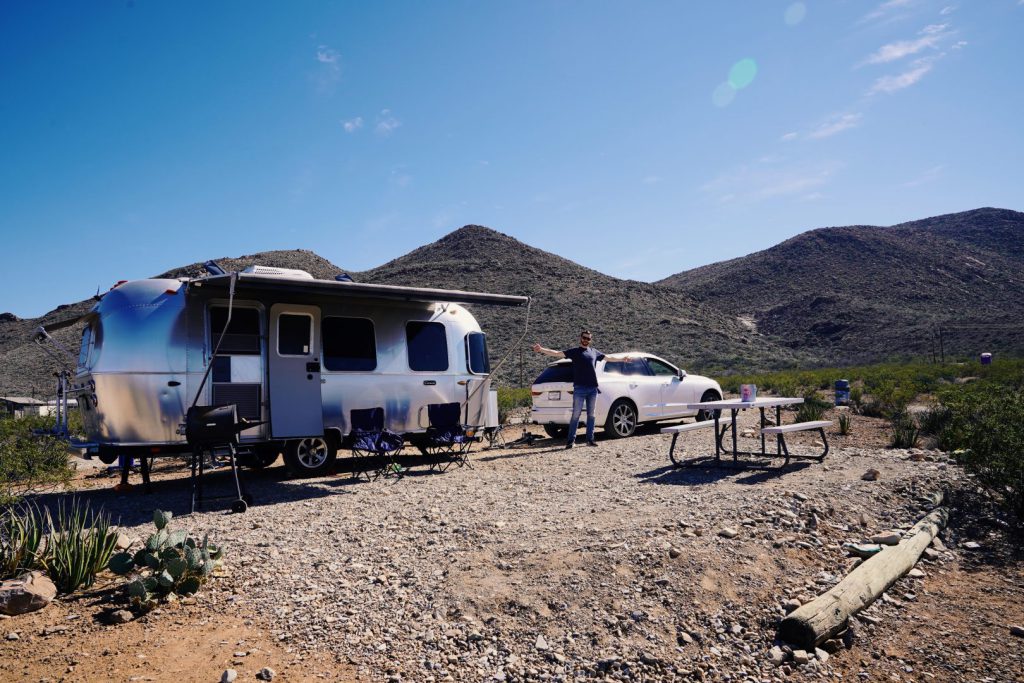 man standing in front of an rv trailer and car near the mountains