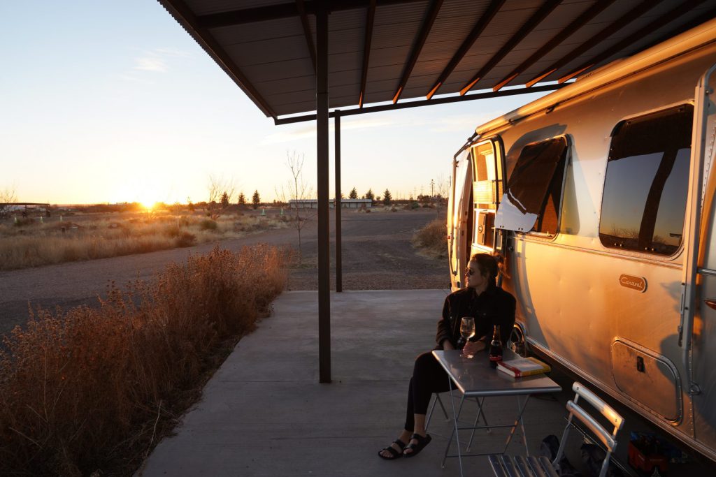 woman sitting outside an airstream trailer with a glass of wine
