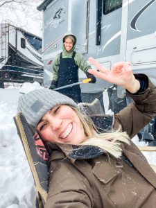 woman smiling in front of an RV on a snowy day