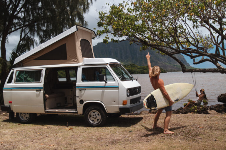 man holding a surfboard next to a campervan