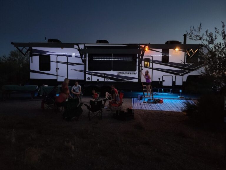 group of people relaxes outside a travel trailer at night