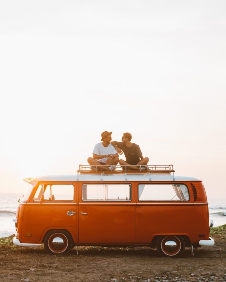 Two men sit on top of a campervan at sunset