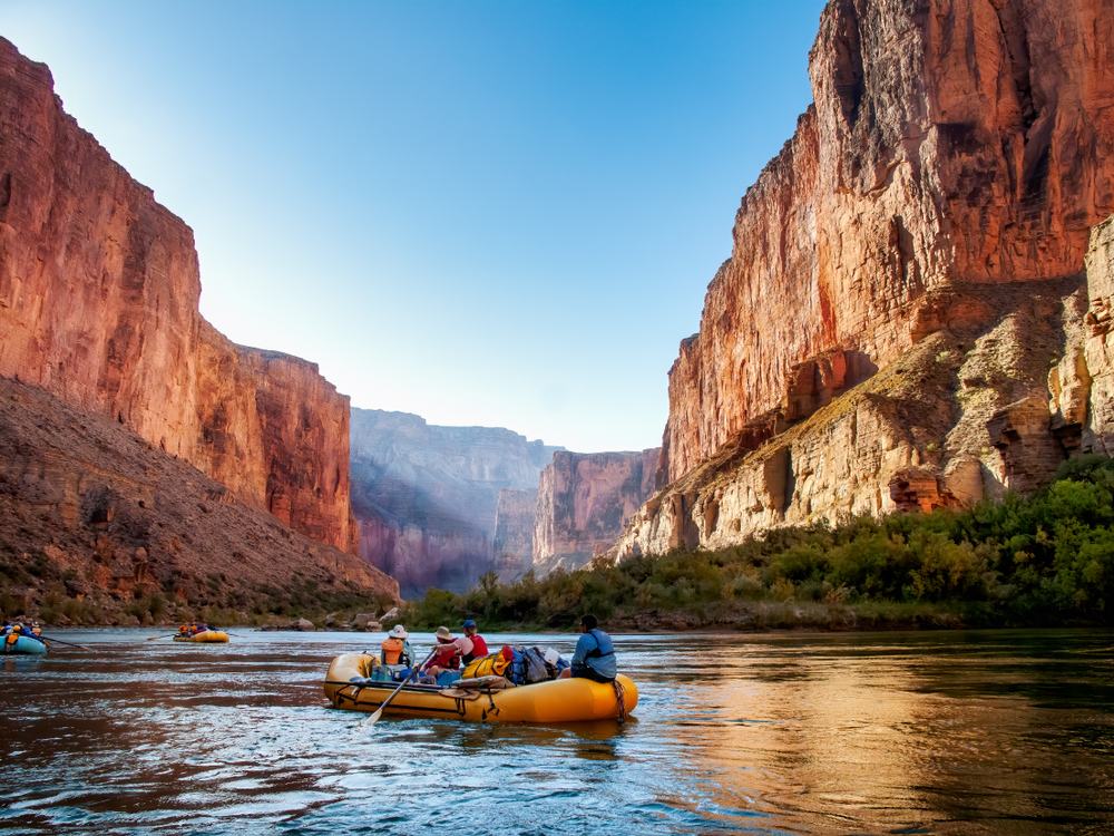 rafters float down the colorado river through the grand canyon at sunrise