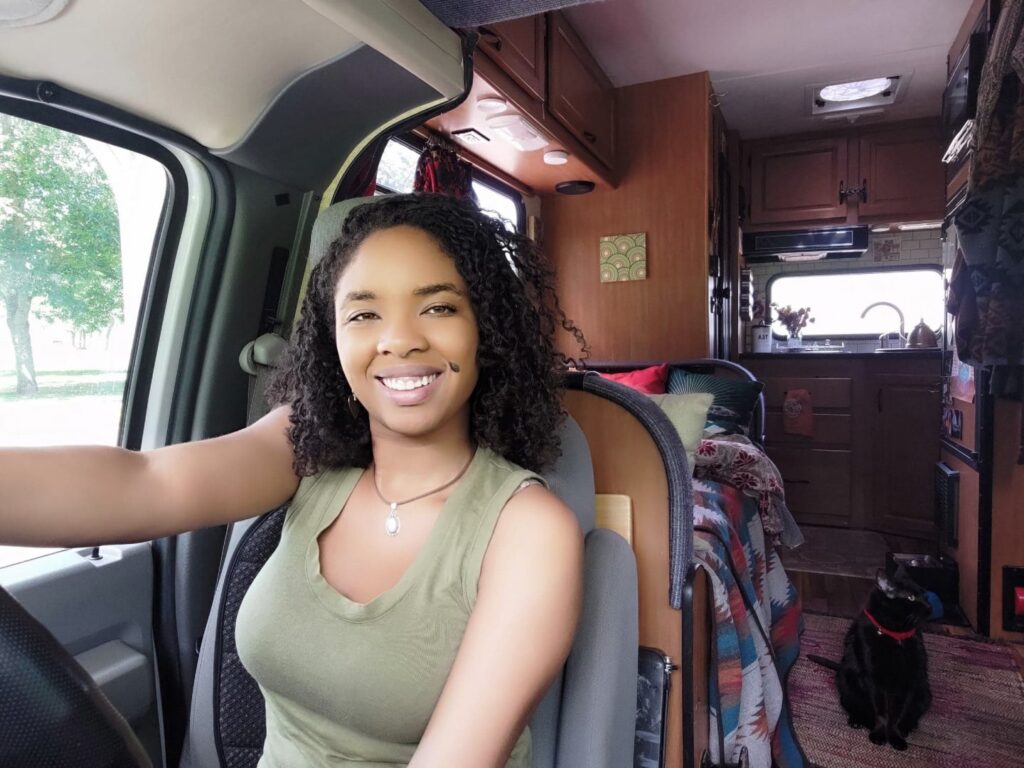 Young woman smiles behind the wheel of her class c rv with her cat in the background