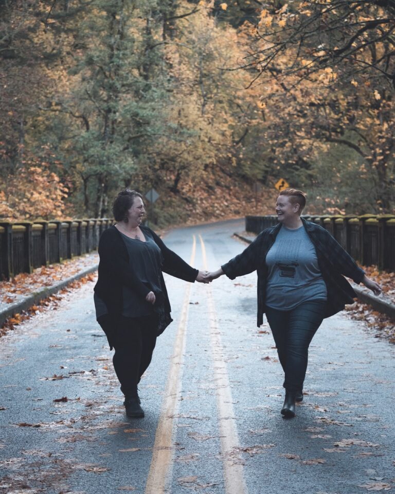 Couple holds hands while walking down the middle of a road, surrounded by fall foliage