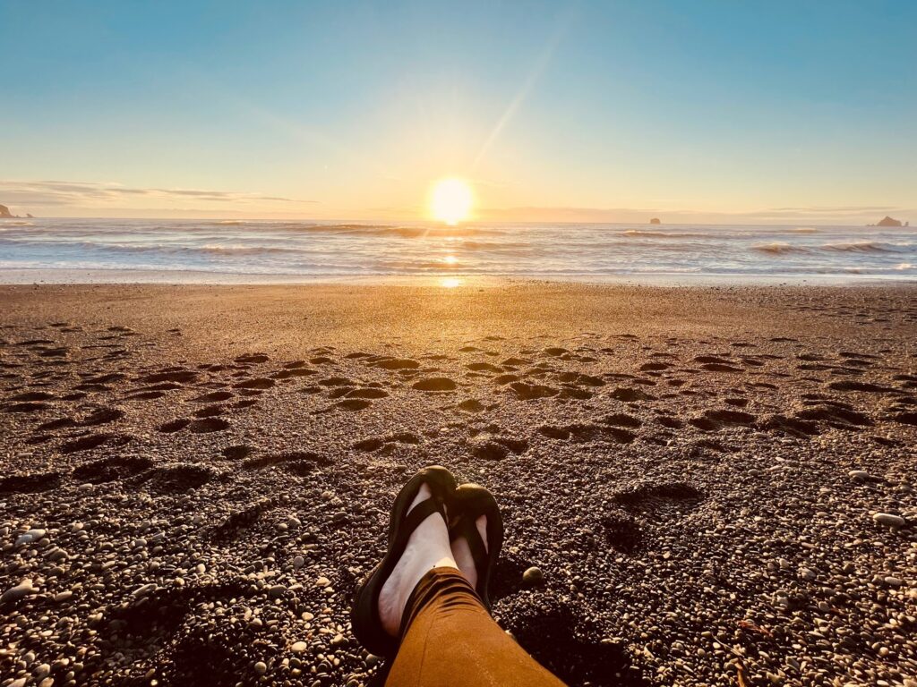 View of legs crossed at the ankle watching the sunset on the coast of the PNW