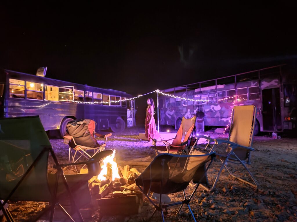 Group of camper friends gather around a campfire in the middle of their parked RVs