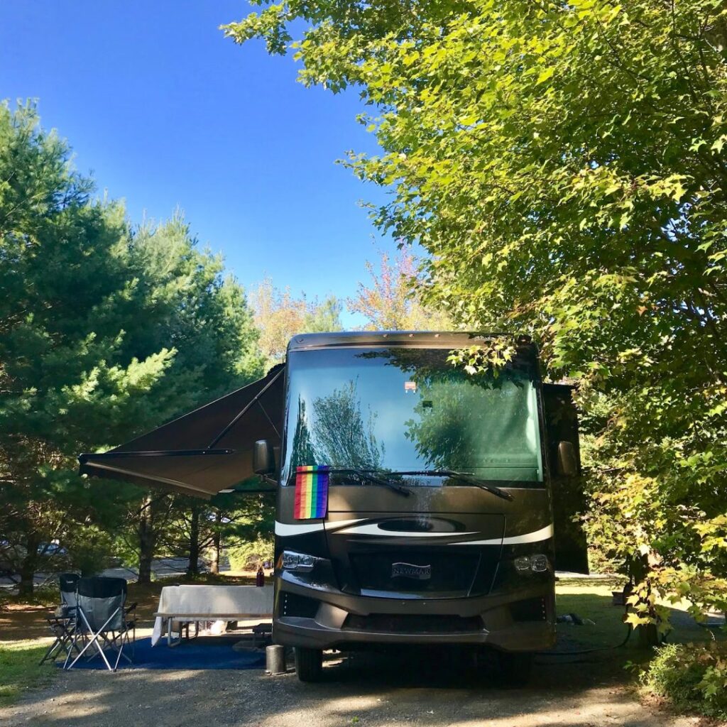 class a rv parked under a tree with pride flag on the windshield wiper