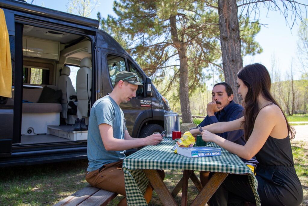 friends playing cards at a picnic table next to a van