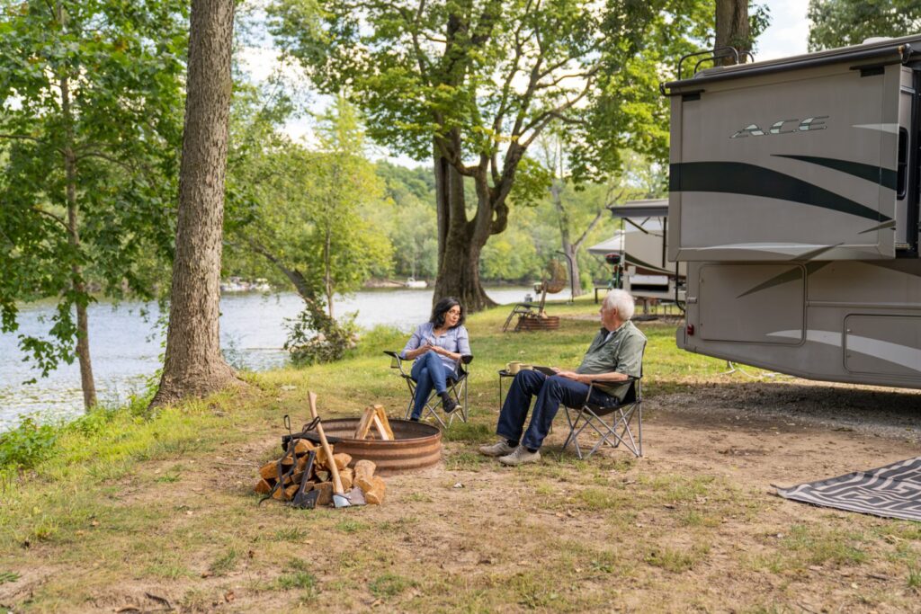 couple sitting in front of a campfire next to their RV and a body of water