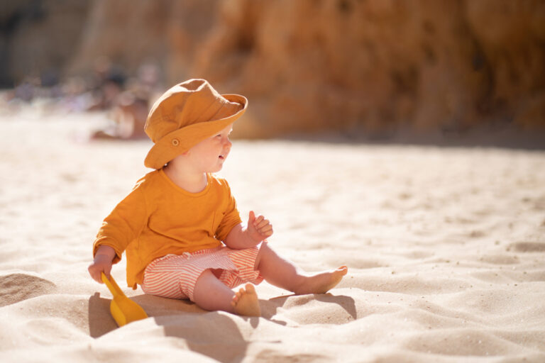 baby wearing a hat sits on the beach