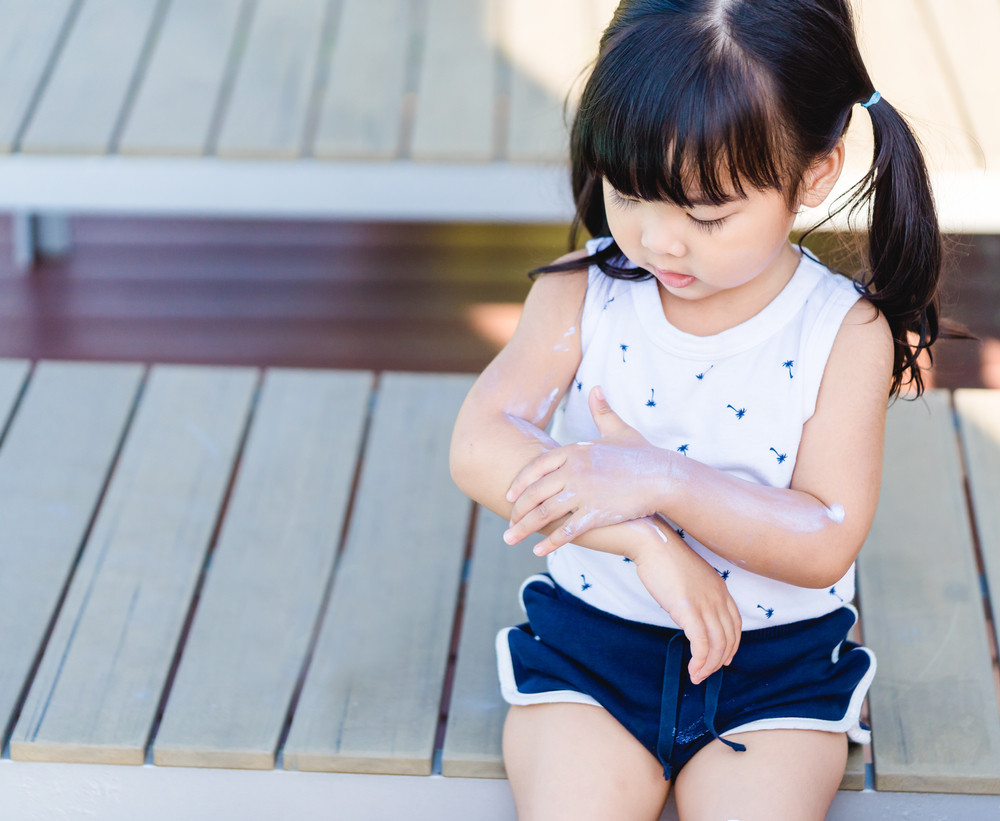 Toddler girl rubs in sunscreen on her arm
