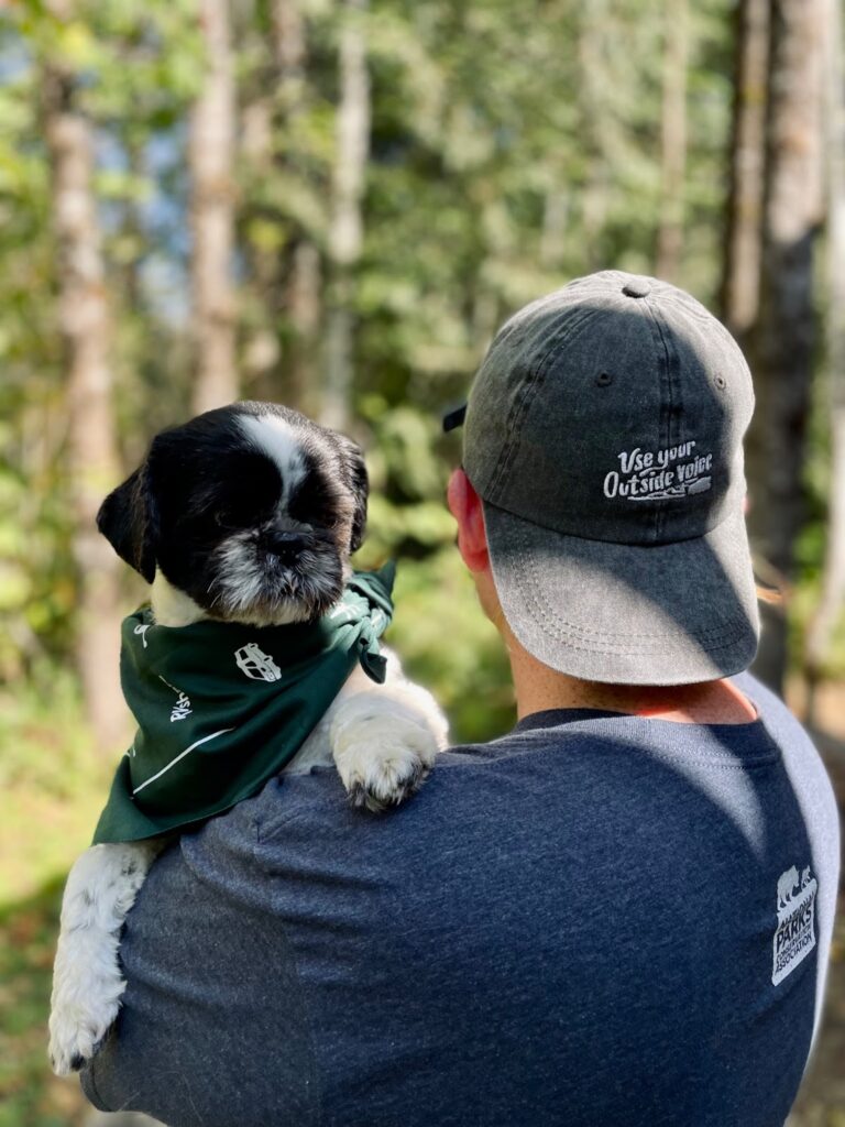 Woman wearing a hat that reads 'use your outside voice' holding a dog who looks over her shoulder