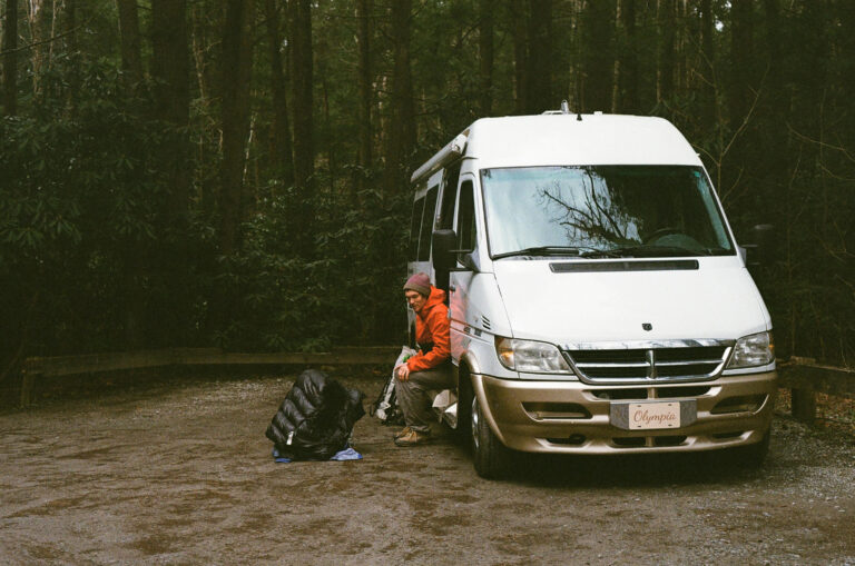 man sitting in door of campervan with pack and jacket