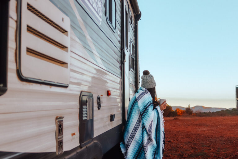 woman standing outside RV with blanket and mug