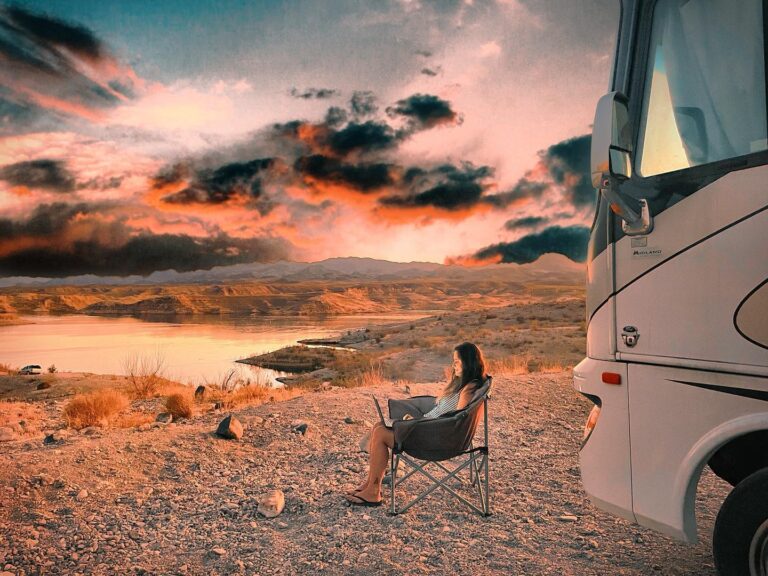 A woman in a camping chair in front of an RV working on a laptop