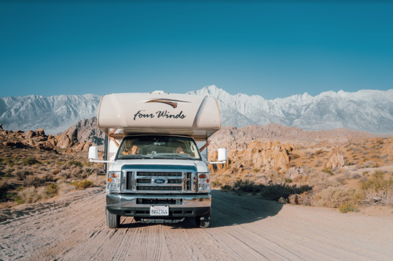 A camper driving down a road with snowy mountains in the distance
