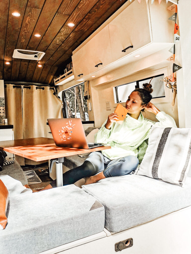 Woman sits at the table of her campervan looking at her phone