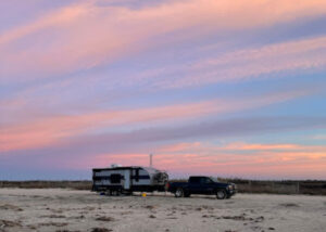 RV travel trailer parked on the beach at sunset