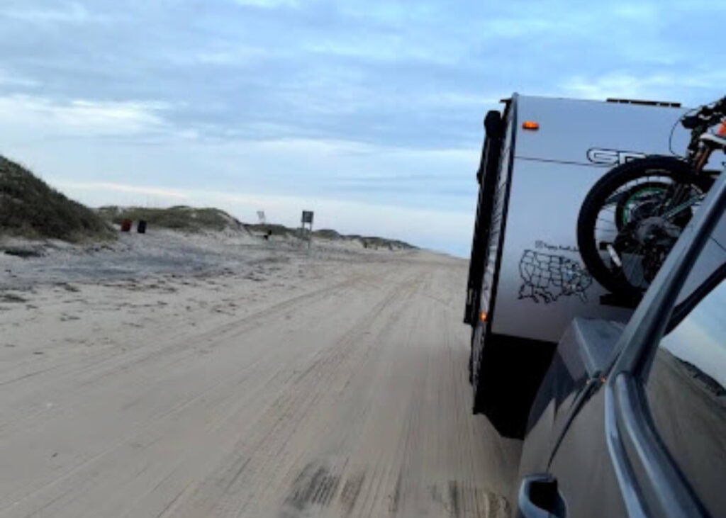 Travel trailer driving down sand road towards the beach. 