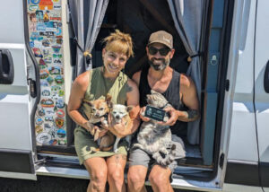 a couple sitting in front of campervan with pets