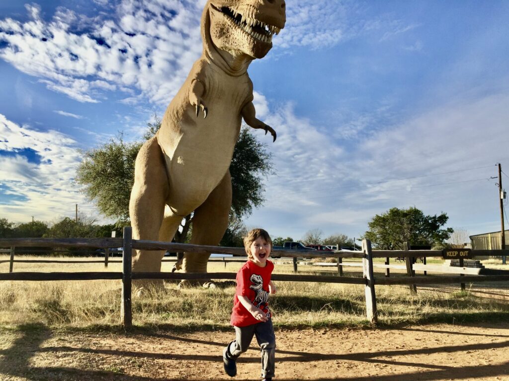 Boy running from dinosaur statue